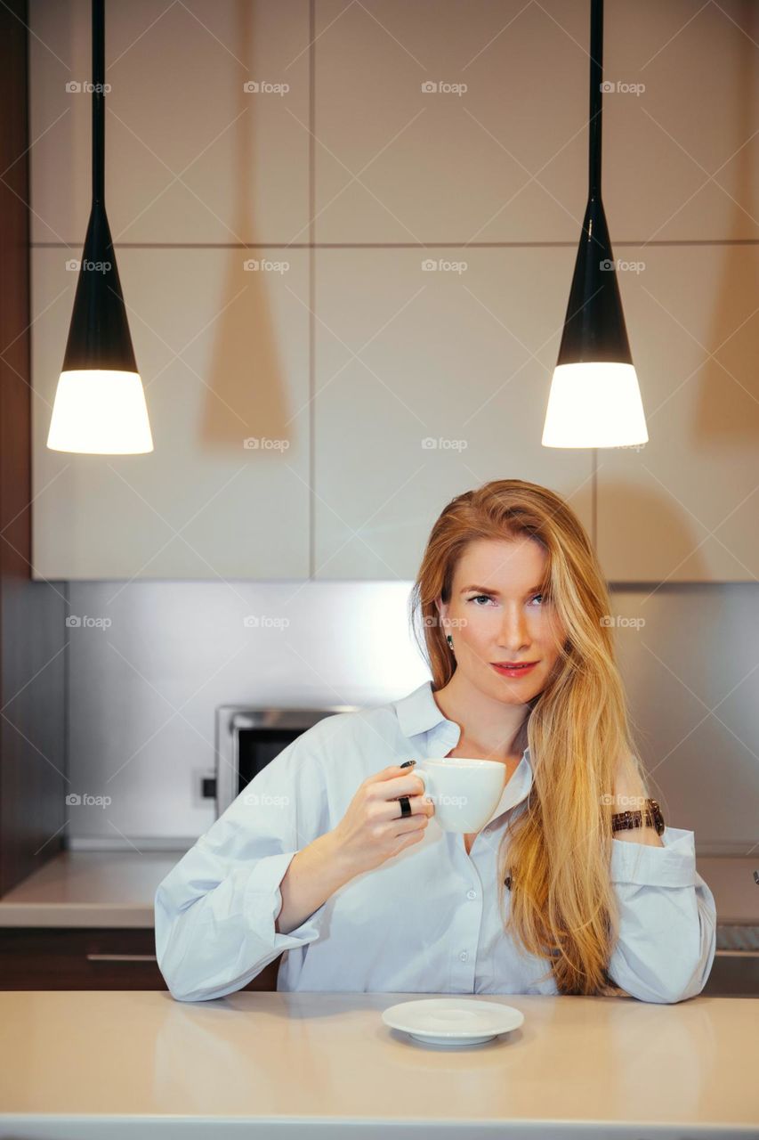 Portrait of young female with long blonde hair, looking at us with a cup of coffee in her hand