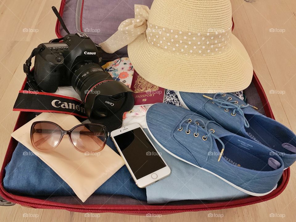 Suitcase with summer clothes, hat, passport, phone, camera, cooling glass and shoes