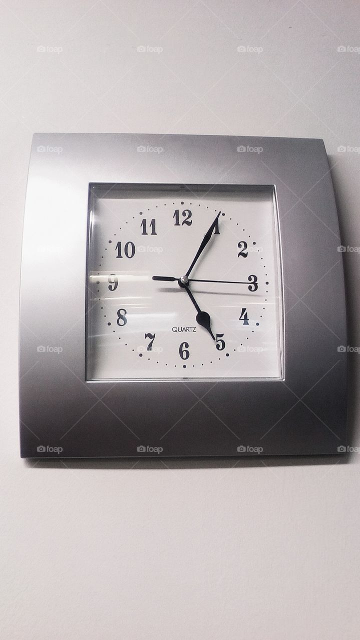 Clock quartz with number and  grey frame hanging on wall in room