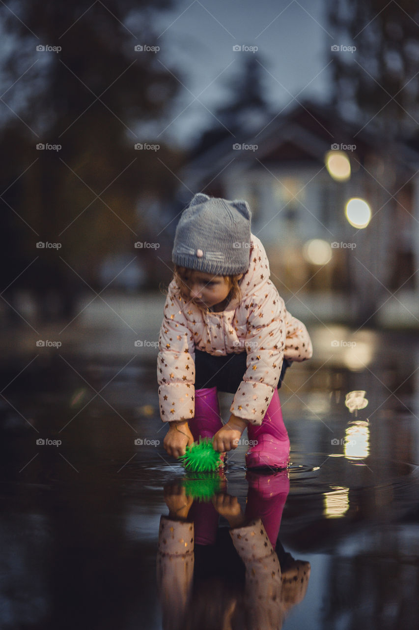 Little girl  in waterproof boots playing in a puddle 