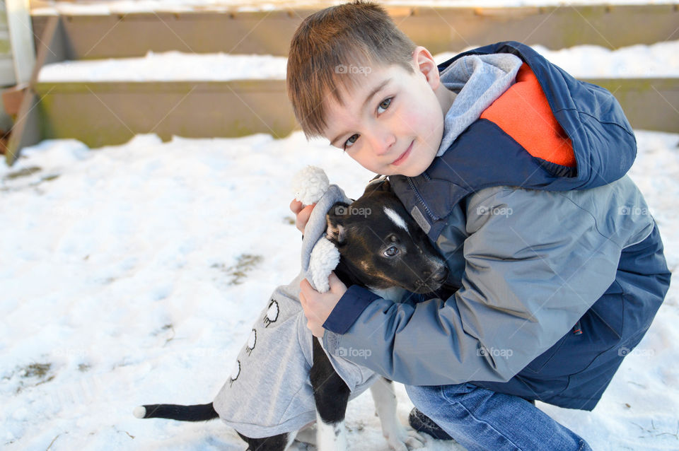 A young boy hugging his new puppy in the snow