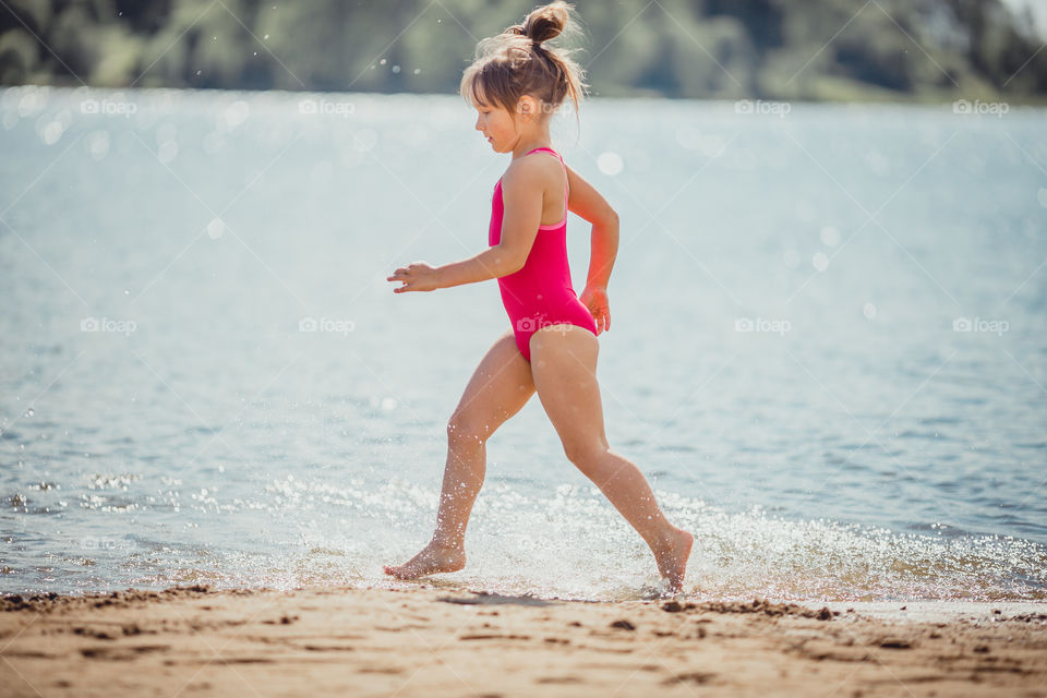 Little girl on lake coast at sunny evening. 