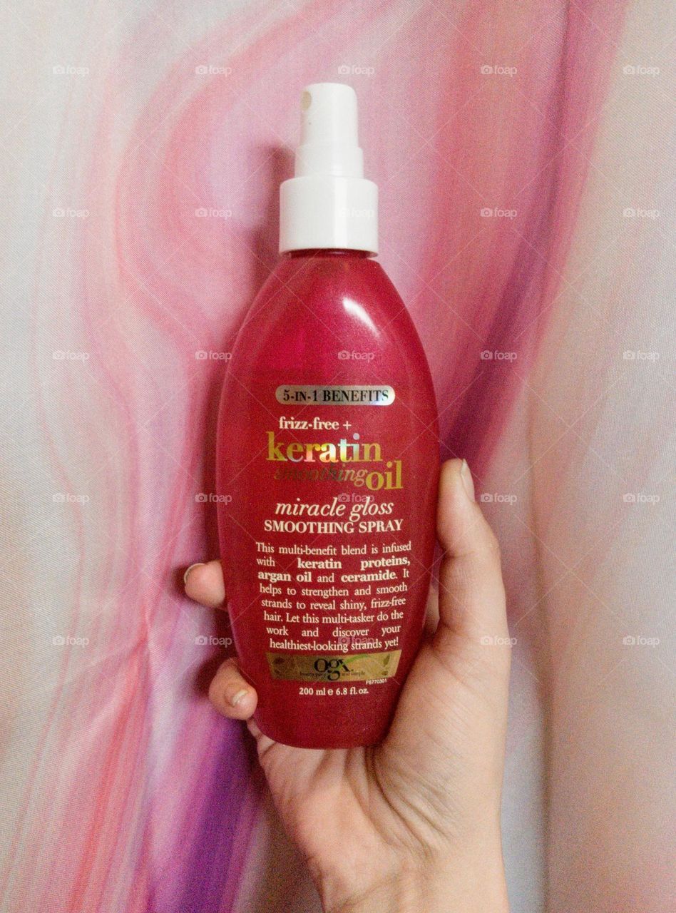 Keratin oil spray for hair against a pink and purple background