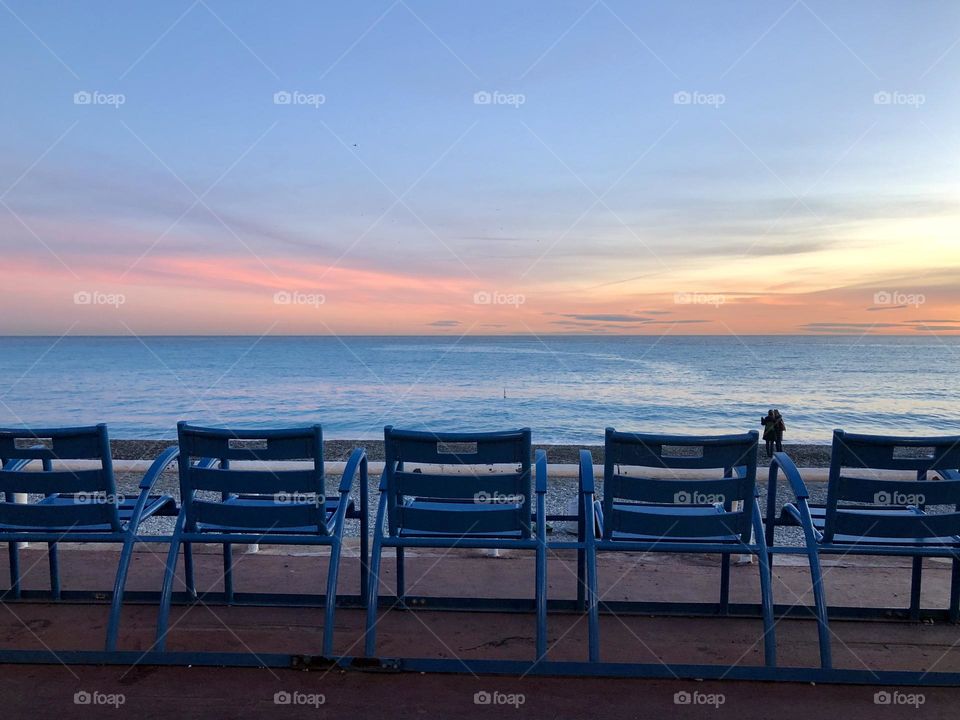 Failure typical blue chairs of Nice, France, aligned in front of the Mediterranean Sea at sunset 