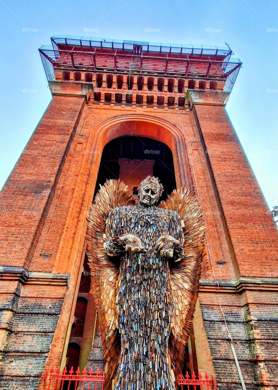 Knife Angel sculpture with backdrop of arch and red brick water tower and blue sky