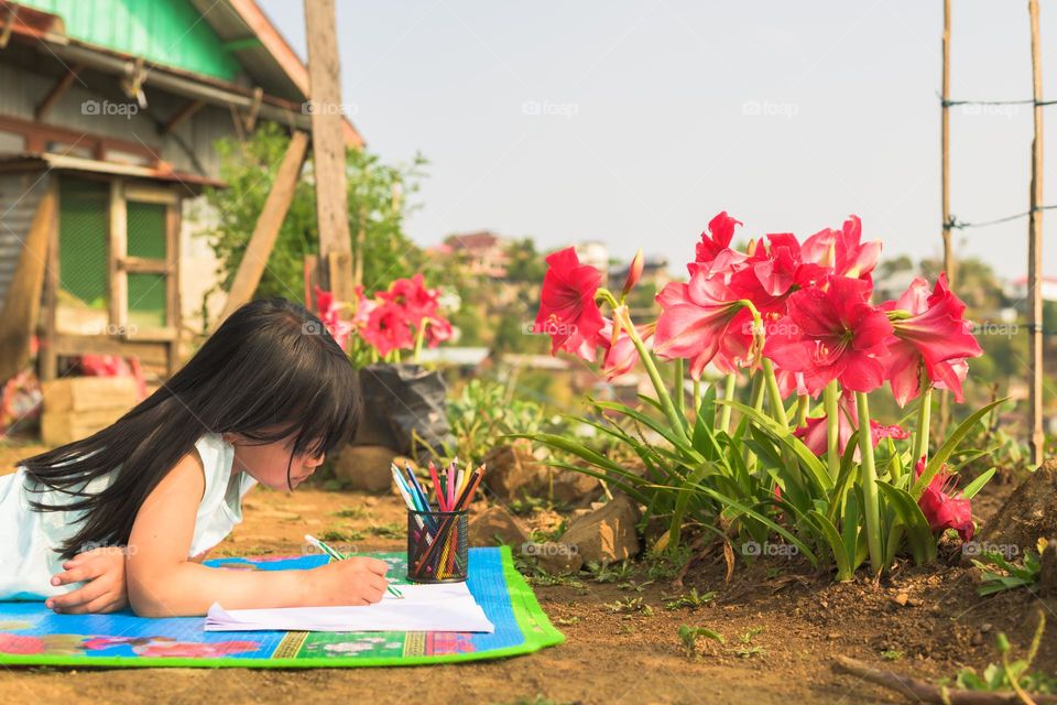 A young little girl getting some inspiration from the spring season, girl drawing flowers in her backyard.