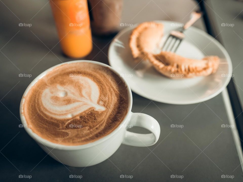 Close-up of coffee latte in a cup with curry puff in the background