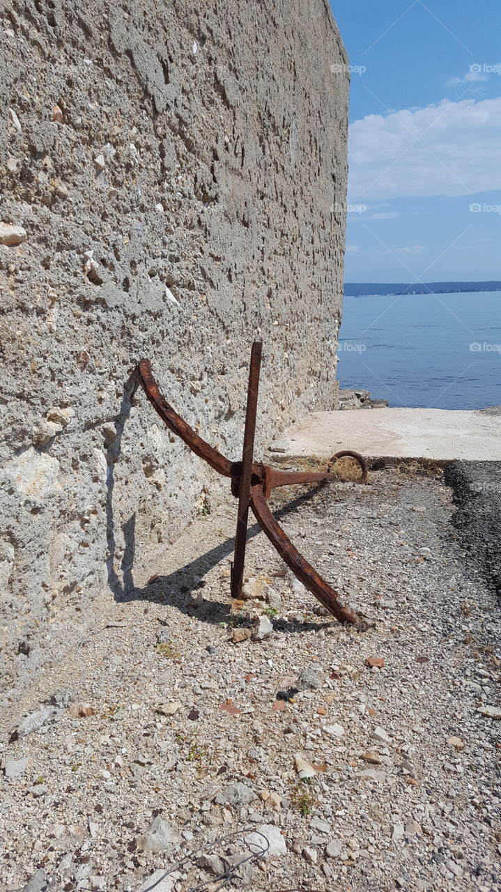 Rusty anchor leaning on a stone wall near the sea