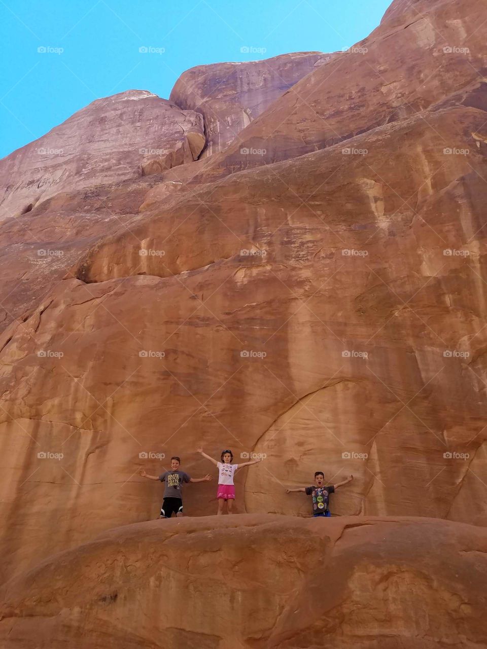 three children halfway up a rock face on the Red Cliffs in Utah 2018