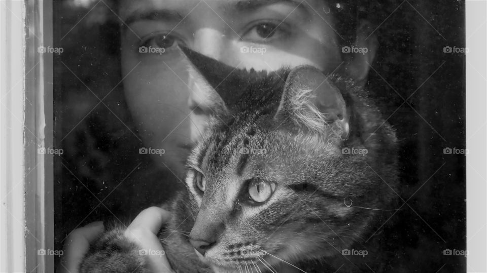 Girl with cat looking out the window in the days of social distancing and isolation