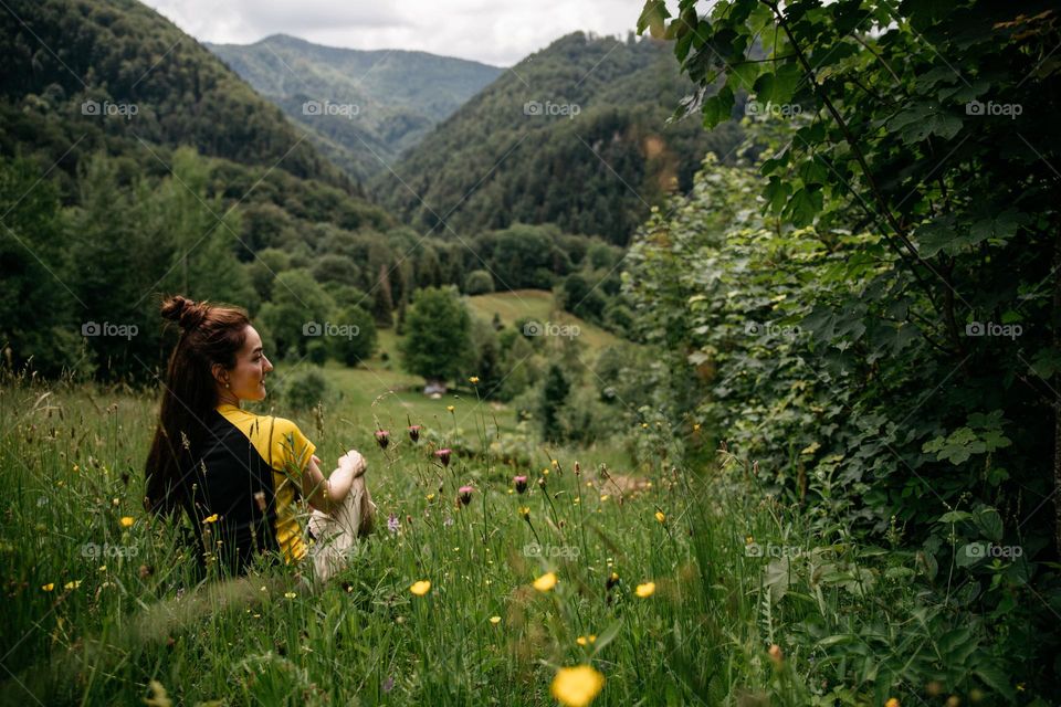 Woman while on a hike, admiring the beautiful green meadow with colorful flowers. 