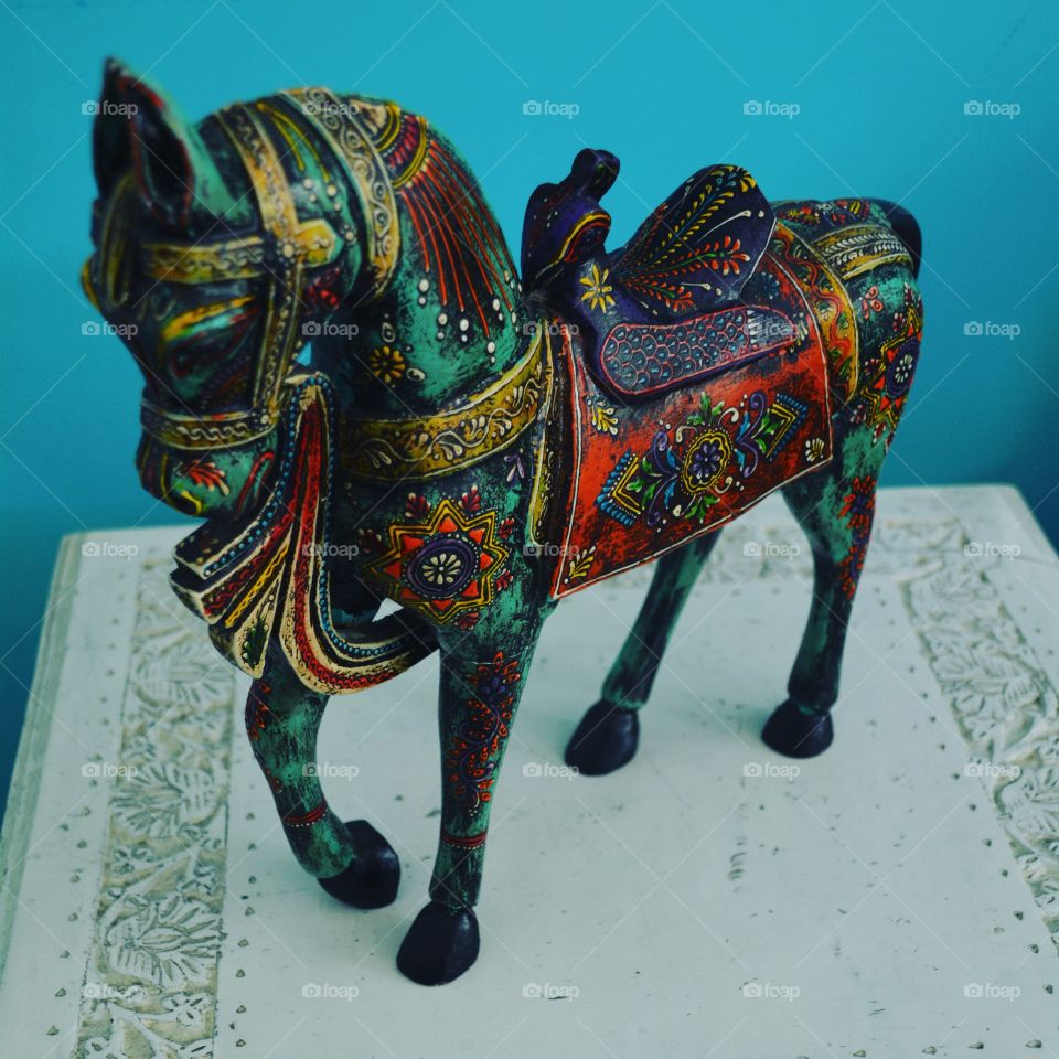 Beautiful handcrafted Indian horse decor in front of blue wall on white side table