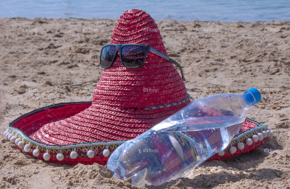 Hat of a sombrero and a bottle of drinking water lies on the beach