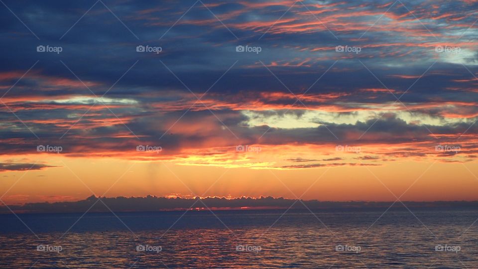 Striking Fiery golden sunset between blue gray clouded sky and dark clouded horizon over gulf of mexico florida