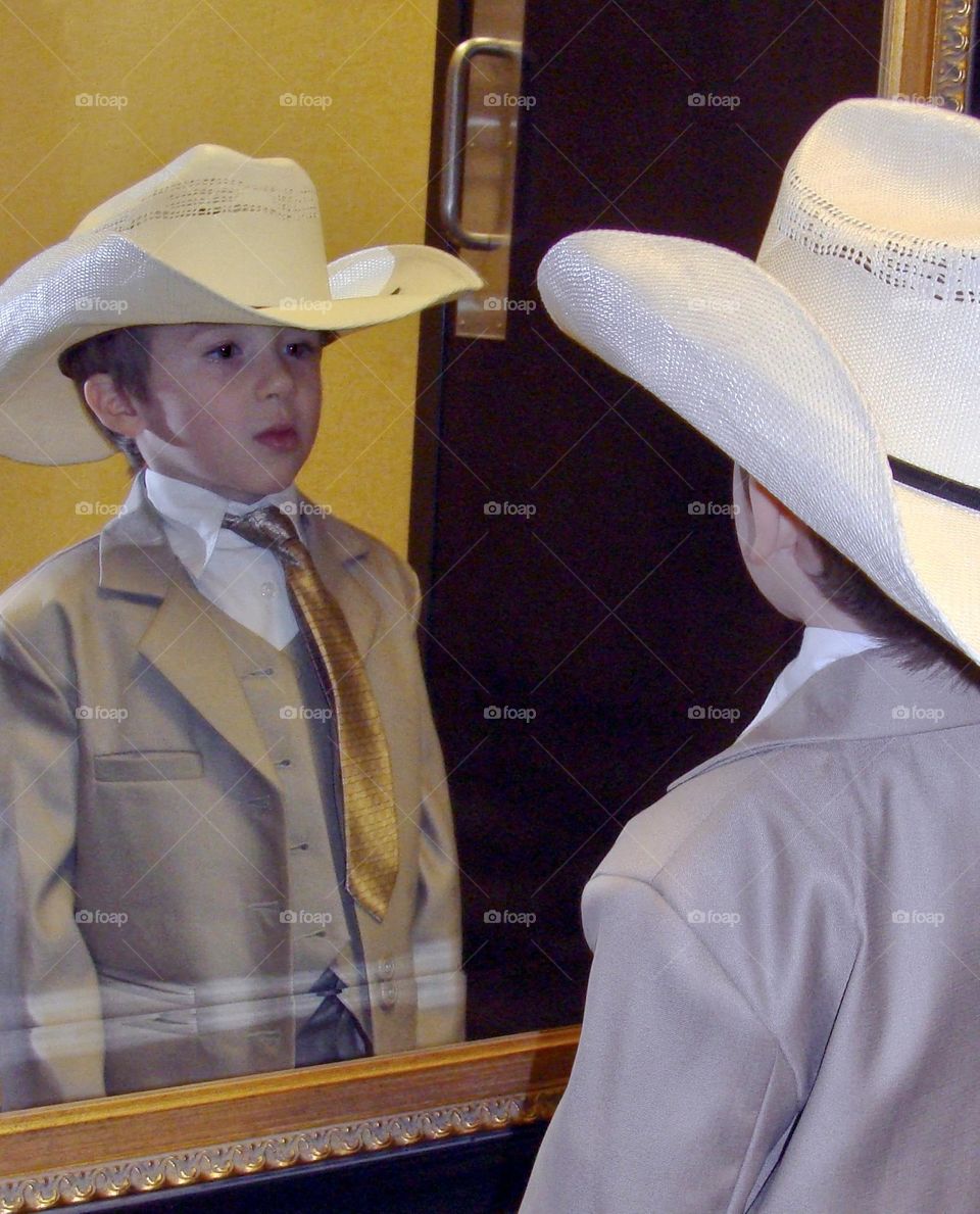 Young boy in cowboy hat looking at himself in a mirror 