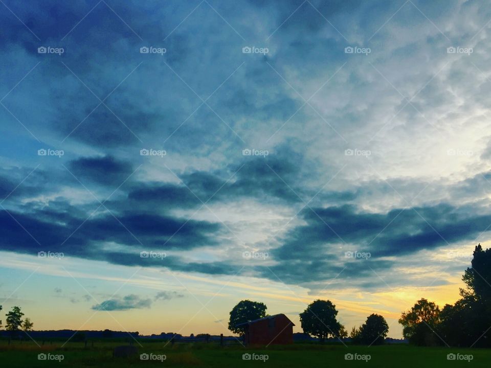 Dramatic Cloudy sky with a soft yellow sunrise over a Countryside landscape showing the silhouettes of trees and sheds