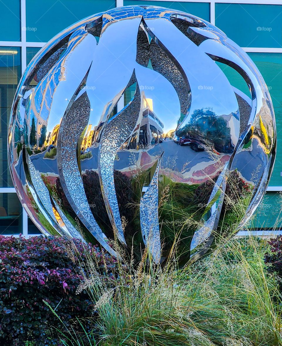A spherical and modern art piece reflects nearby buildings in a commercial roundabout