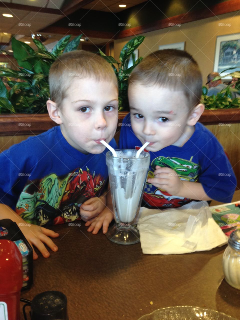 Two brother drinking juice with straw in restaurant