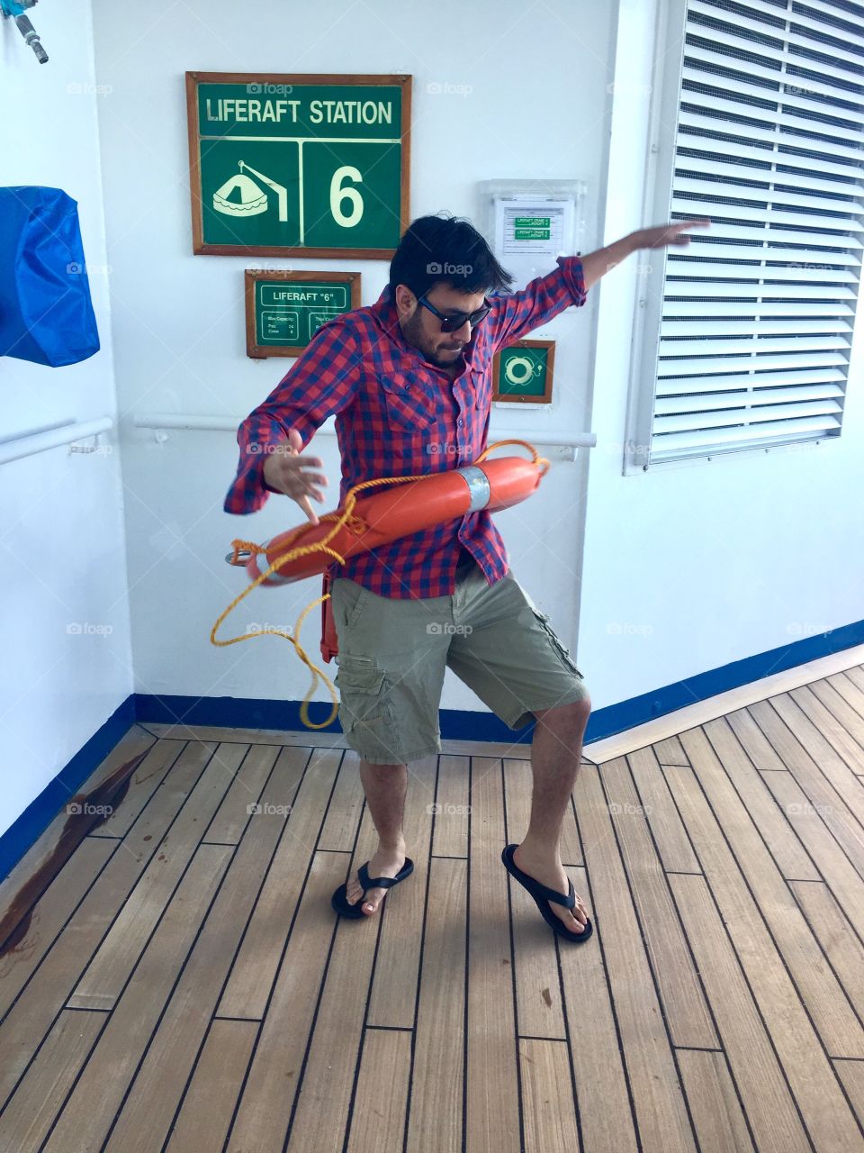 Guy in a gingham red shirt hula hooping with an orange lifesaver floatation device on a cruise ship