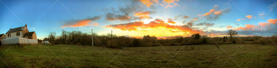 A panoramic view of the winter sky at sunset, a traditional farmhouse can be seen on the left