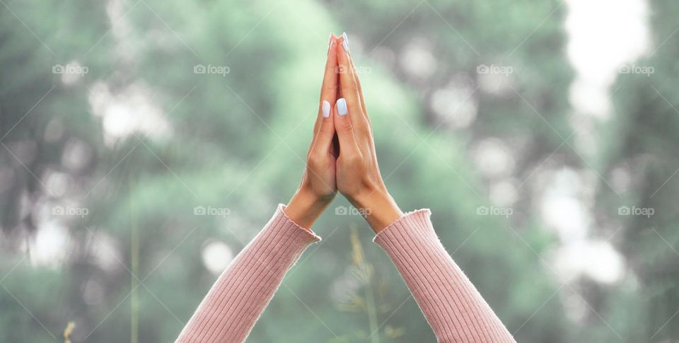 Close-up of hands joined together in a namaste gesture against a backdrop of nature. Mental health and wellbeing concept.