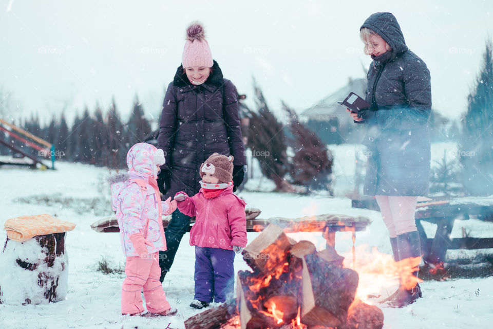 Family spending time together outdoors in the winter. Parents with children gathered around the campfire preparing marshmallows and snacks to toasting over the campfire using wooden sticks