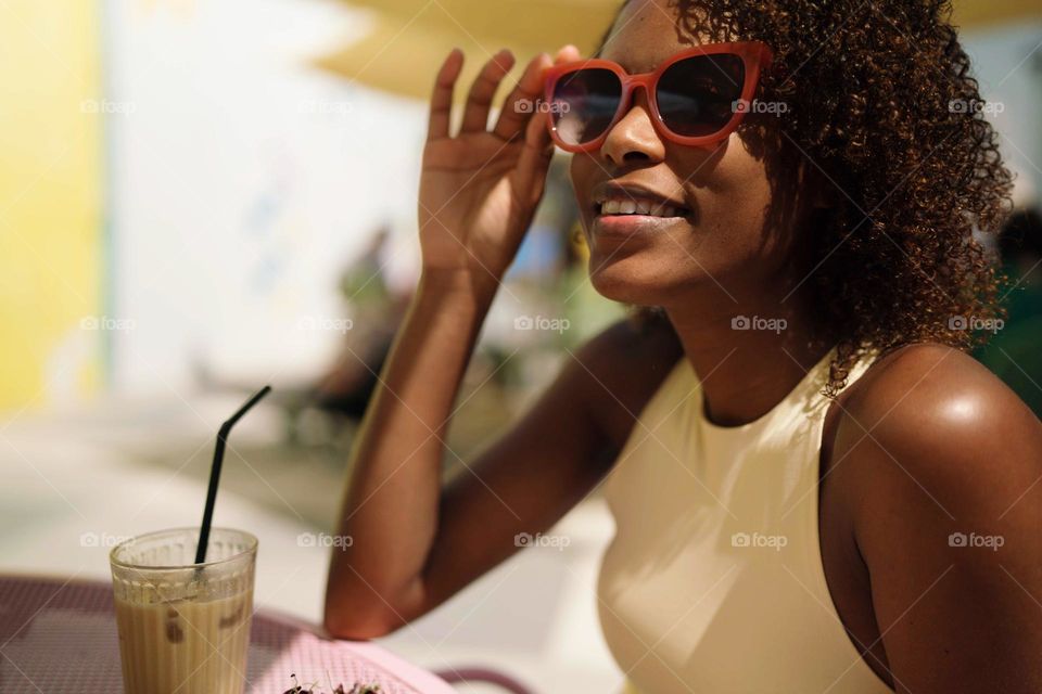 Beautiful black woman with Afro hair having avocado toast and iced coffee for breakfast in the outdoor cafe