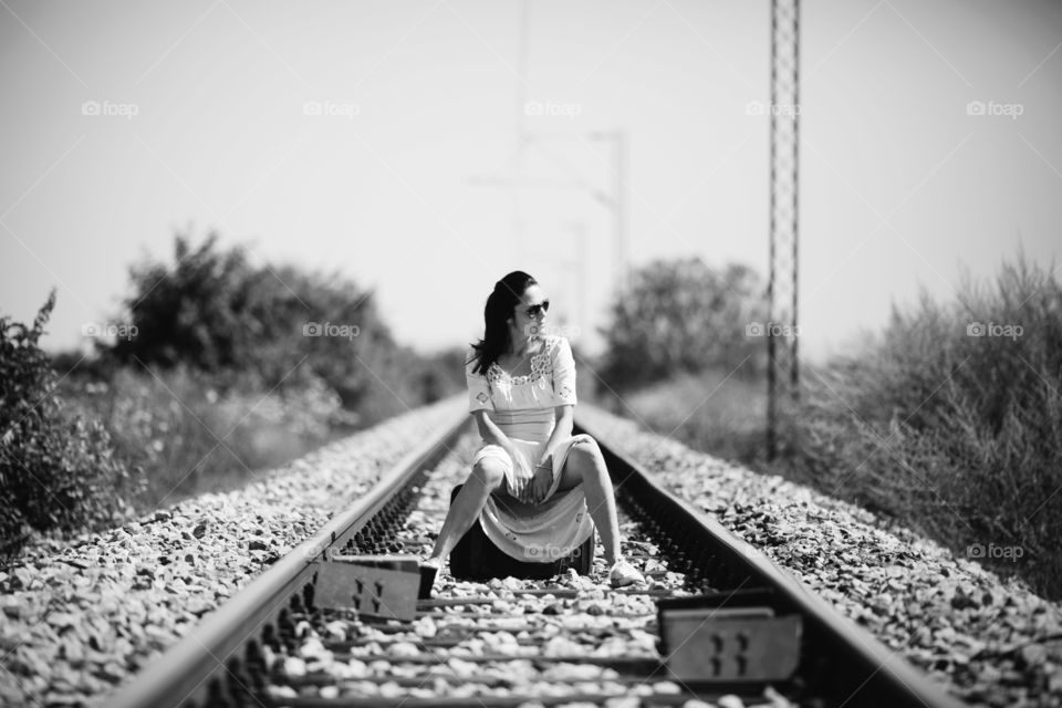 Woman sitting on a suitcase on the railtracks