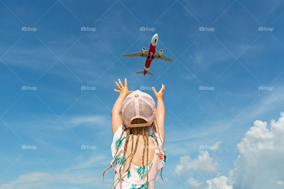 Little girl with blonde hair from behind and aircraft flying 