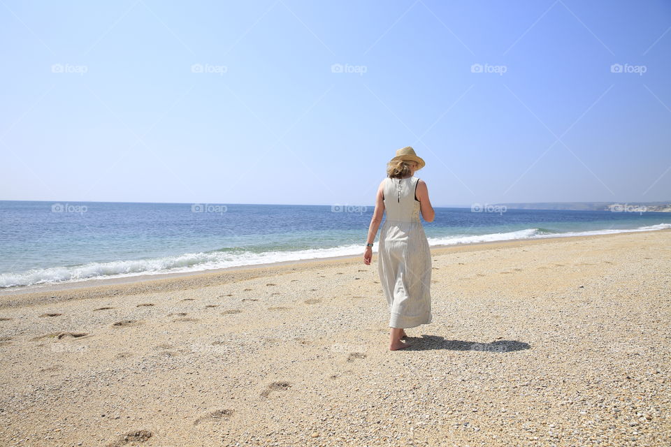 A single woman walking along a deserted beach on a hot summer day