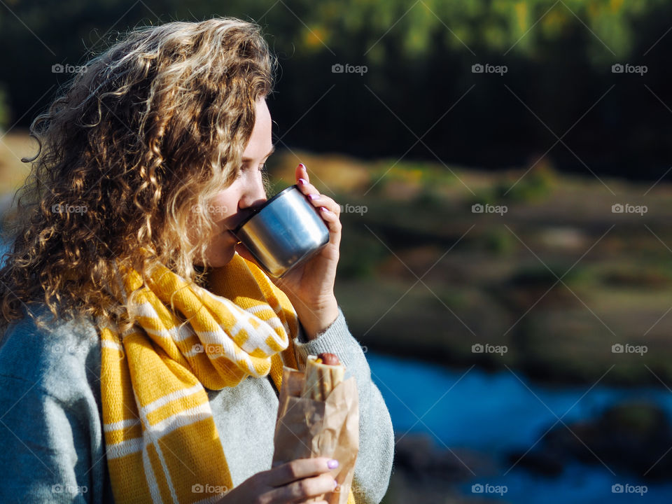 Young curly woman in sweater and scarf drinking hot tea