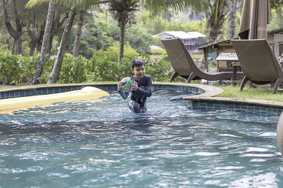 Asia boy holding the ball in a swimming pool.