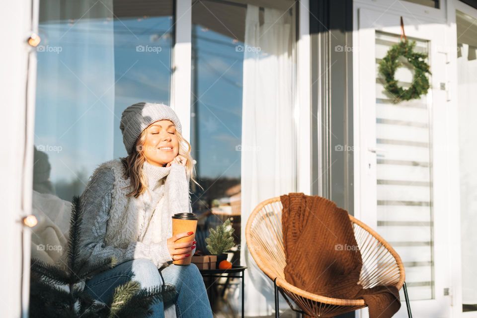 Beautiful woman with cup of hot drink near house in winter season 