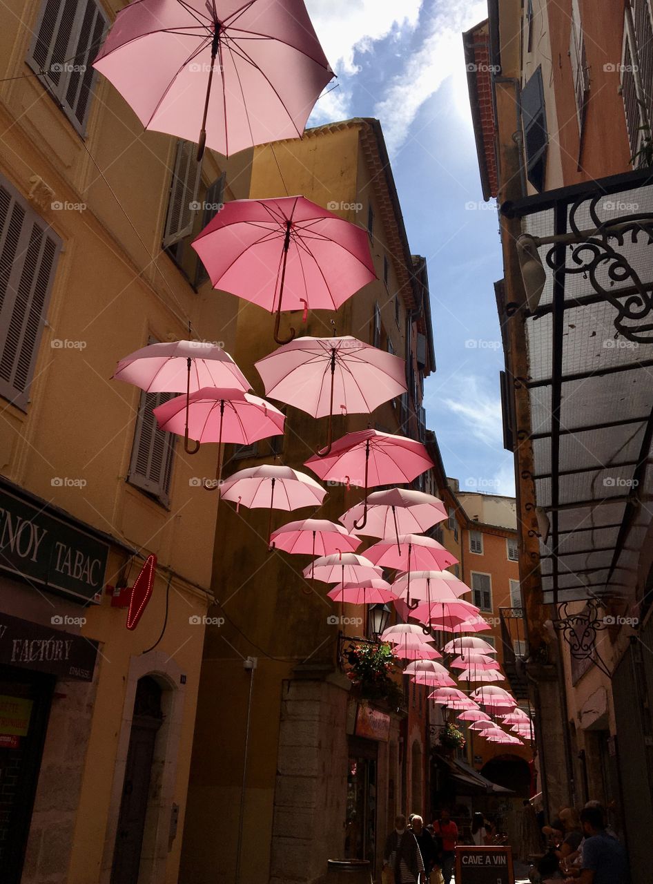 Pinky umbrellas against sunshine in historic streets of Grasse