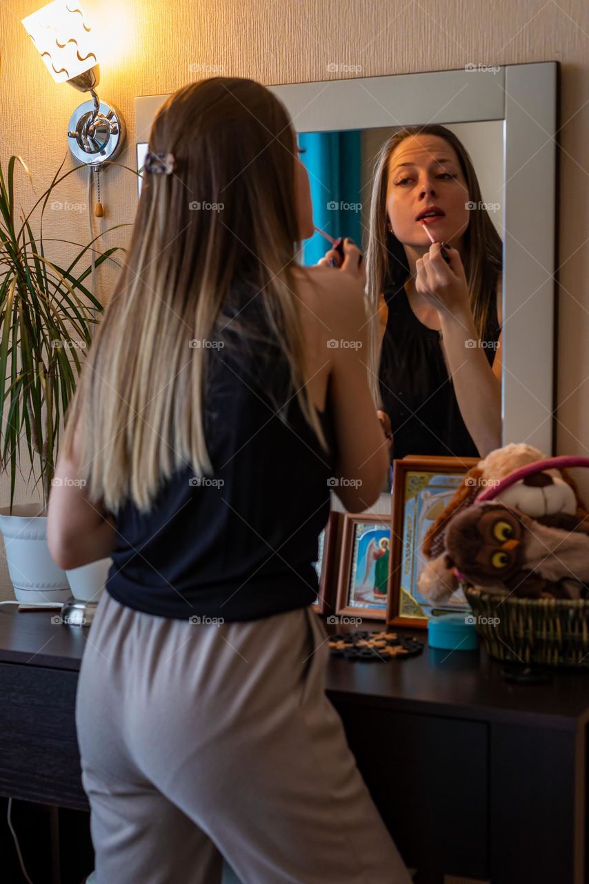 Home beauty salon woman paints her lips looking in the mirror