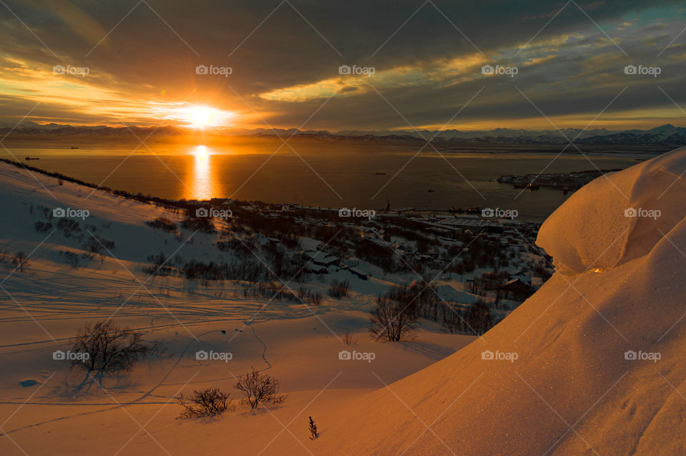 Kamchatka is a snowy hillside lit by the sun during sunset.  Avacha Bay, Pacific Ocean