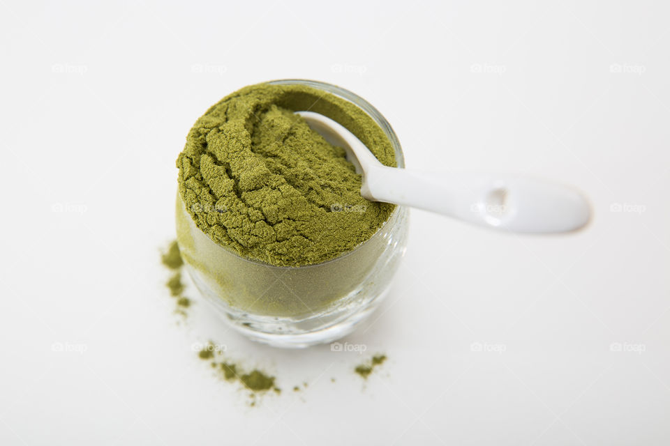 Product wheat grass powder in glass with white spoon isolated on pure white background.