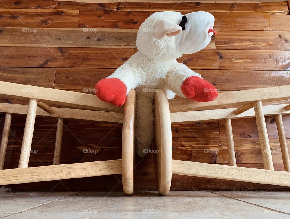 Sheep Or Lamb Plushie Toy For Kids And Dogs Between Symmetric Two Bar Stools Laid Down. It Seems To Be Looking Outside From The Inside On It’s Left Side.