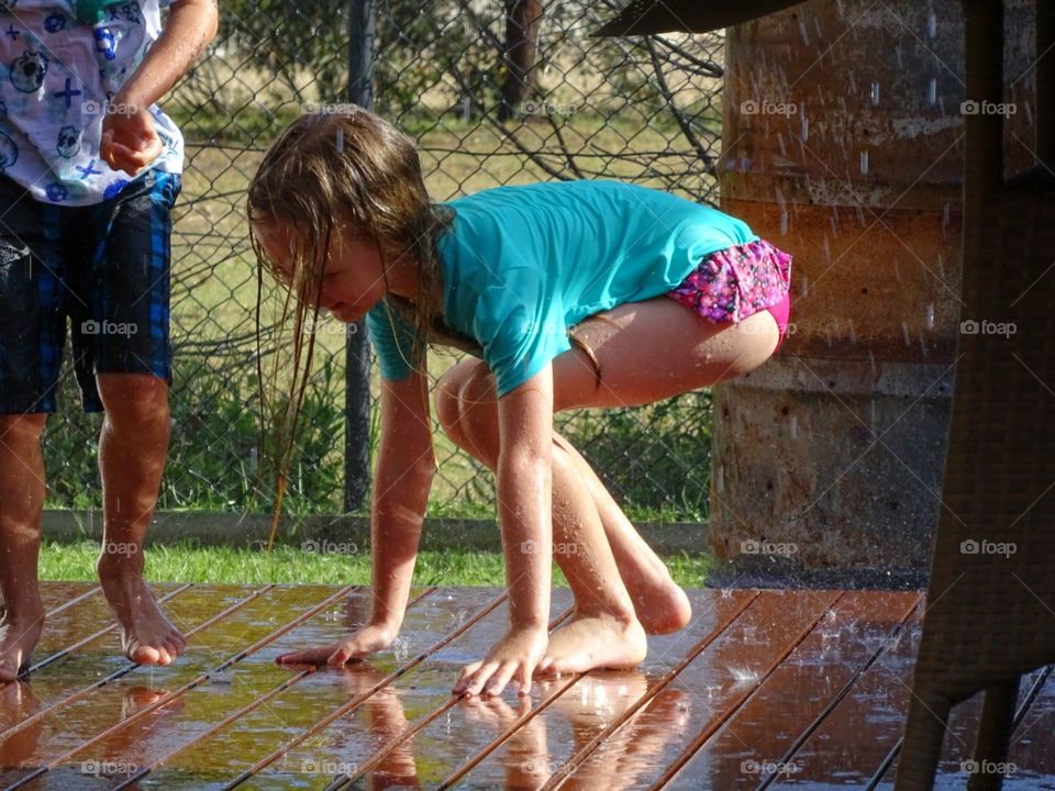 girl and boy playing in the backyard with the hose and water having fun together on the wet deck
