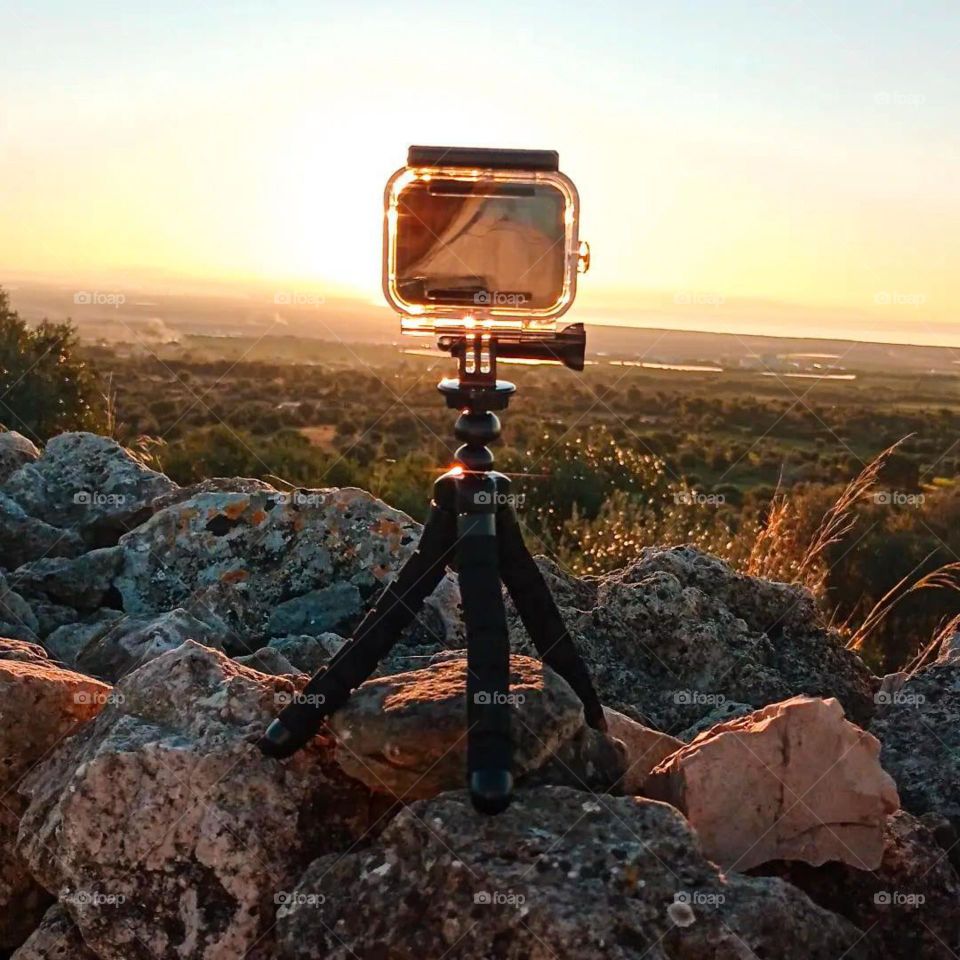 Portrait of an action camera placed on a tripod, placed on a rock with a sunset and beautiful natural scenery in the background