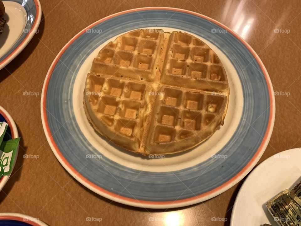 A whole round Waffles on a round light blue plate for breakfast and brunch. Fresh.