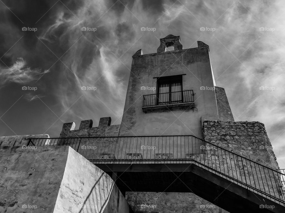 Beautiful view of the historical ancient rectangular wall with square windows and the iron black staircase of the ancient castle in the city of Culleoa, Spain, close-up view from below. The concept of the architecture of ancient castles.