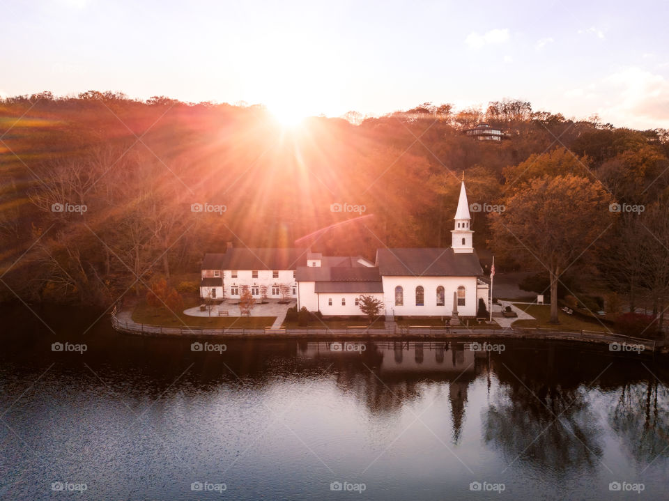 Beautiful white church reflecting in a lake, with the sun rising over the mountain in the background causing a bright sun flare.