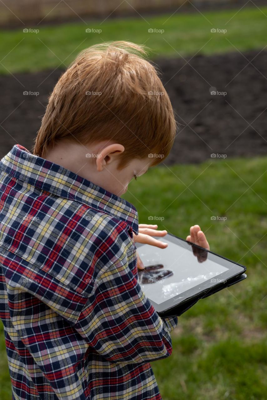 Red-haired boy watching a movie on a tablet with a garden