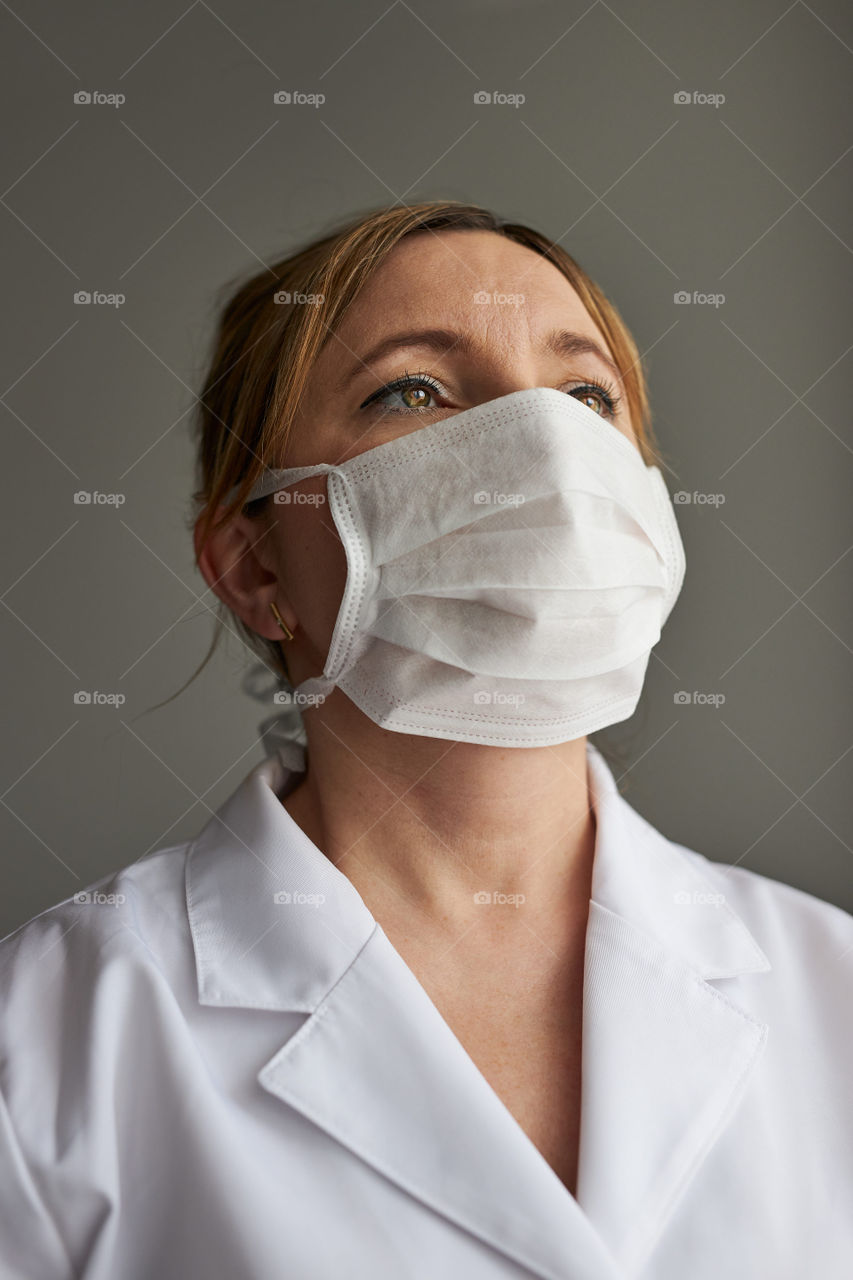 Doctor with face covered with mask. Portrait of young woman wearing the uniform, cap and mask to avoid virus infection and to prevent the spread of disease. Real people, authentic situations