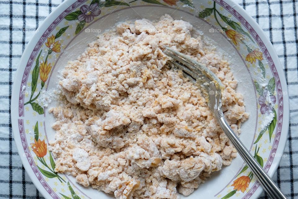 A bowl with dough for American peanut butter cookies and fork on checkered napkin