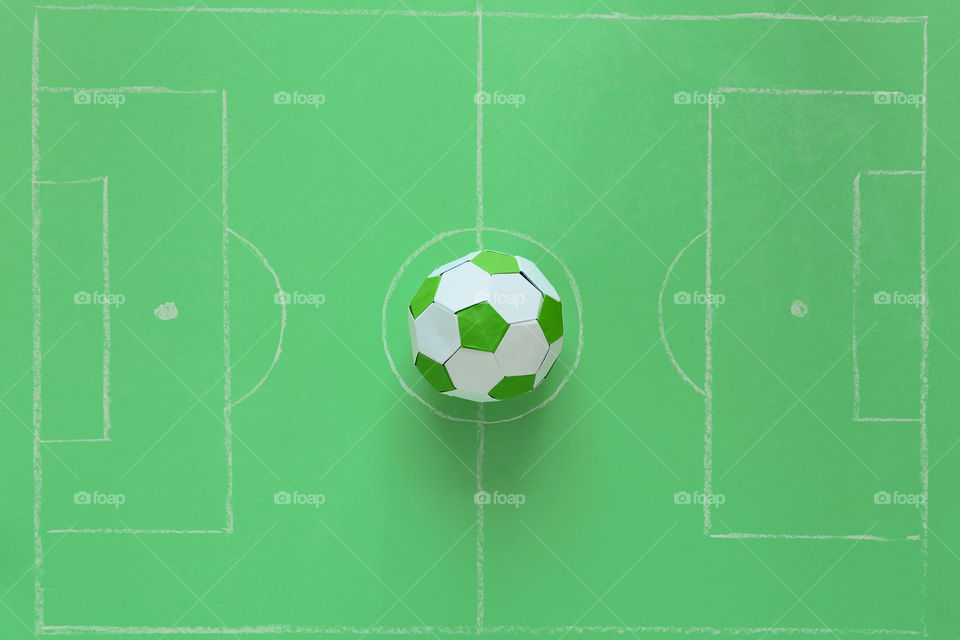 Paper soccer ball on soccer field or green background. Origami. Paper craft. Soccer game concept.