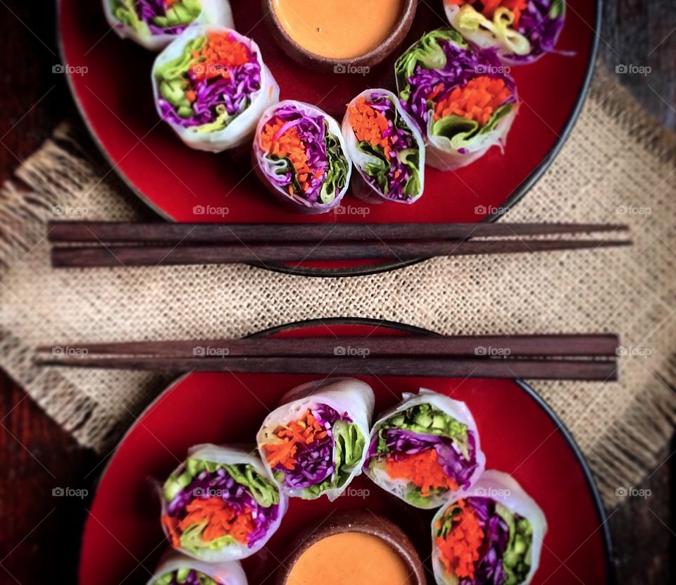 Colorful Vegetarian summer rolls on a red plate with dipping sauce and chopsticks. 