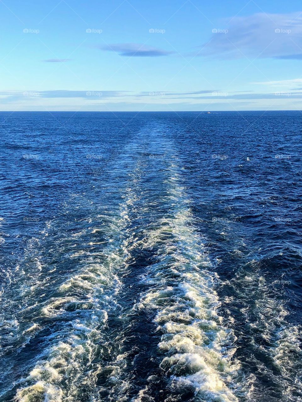 Tranquil scene with long ship trail and far horizon over water under light blue sky