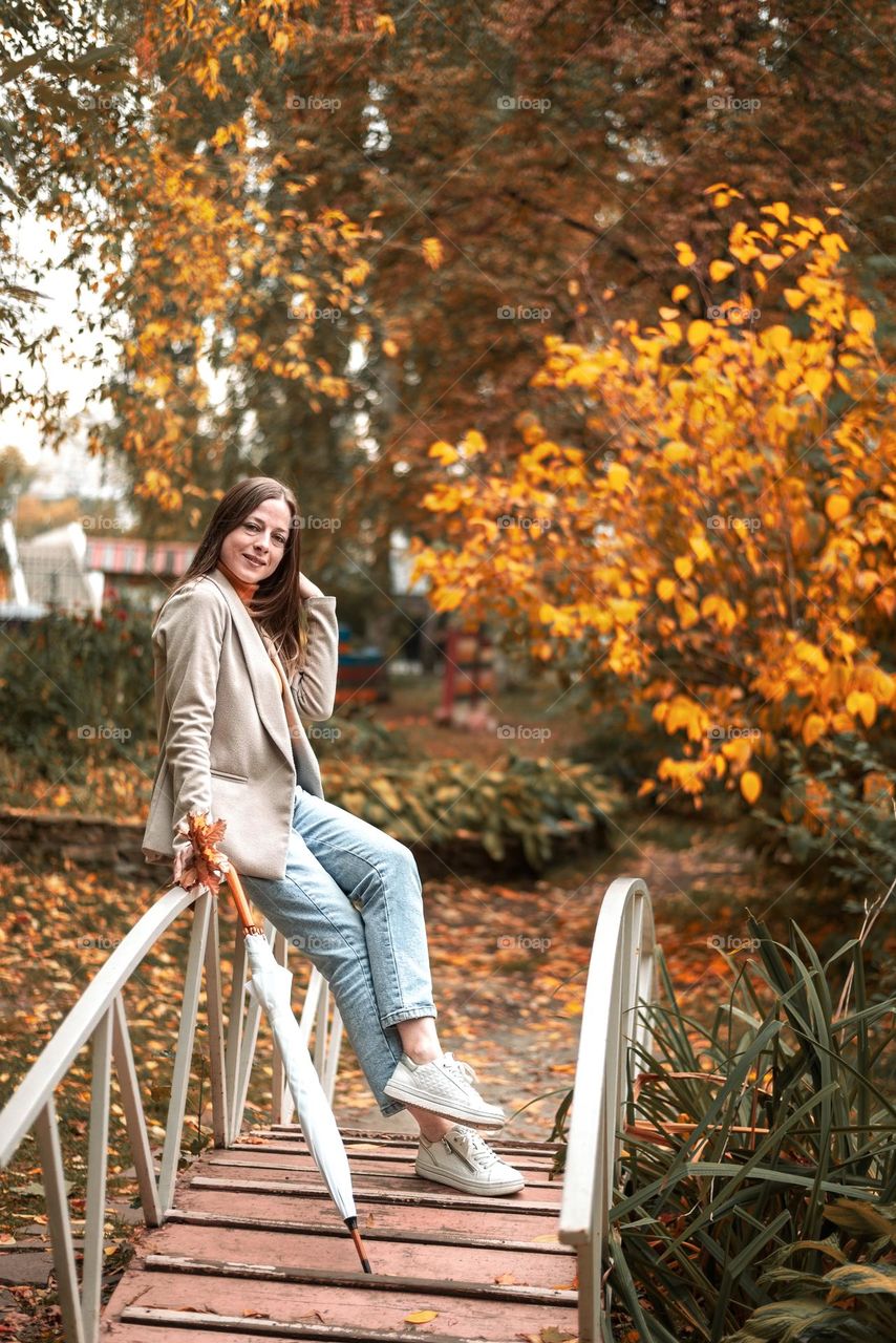 Beautiful girl on the bridge in the autumn park with an umbrella, walking outdoors